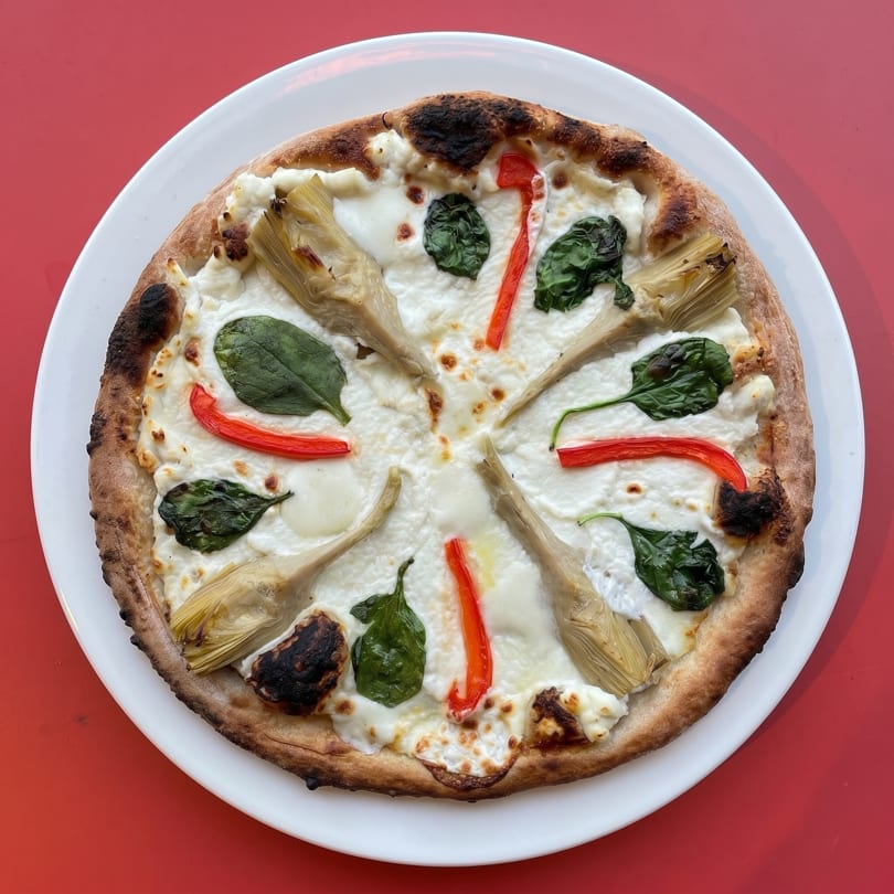 White pizza with artichoke hearts, red peppers, and spinach on a white plate.