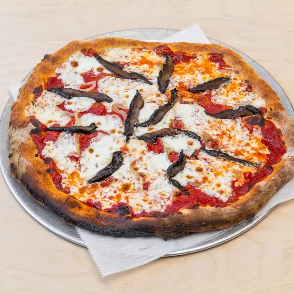 A whole pizza with tomato sauce, melted mozzarella, onions, and dark mushroom slices on a metal tray.