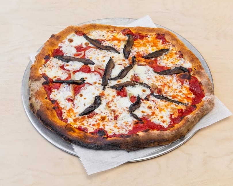 A whole pizza with tomato sauce, melted mozzarella, onions, and dark mushroom slices on a metal tray.