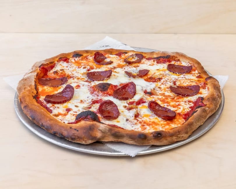 A whole pepperoni pizza with melted cheese and a crispy crust on a metal pan.